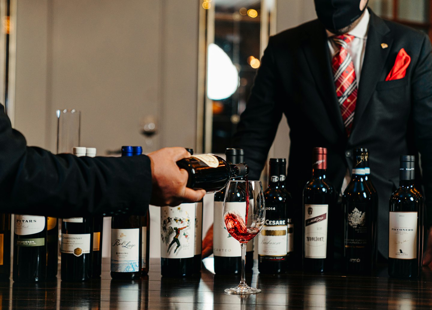 Sommelier sirviendo vino tinto en una copa sobre una mesa.